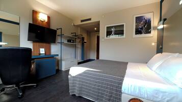 A hotel room with a bed, a desk with a chair, a television, and a wardrobe.
