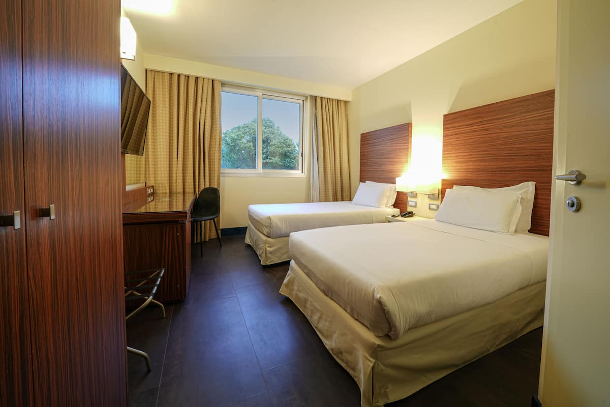 A hotel room with two beds, a desk, a chair, and a window with curtains.