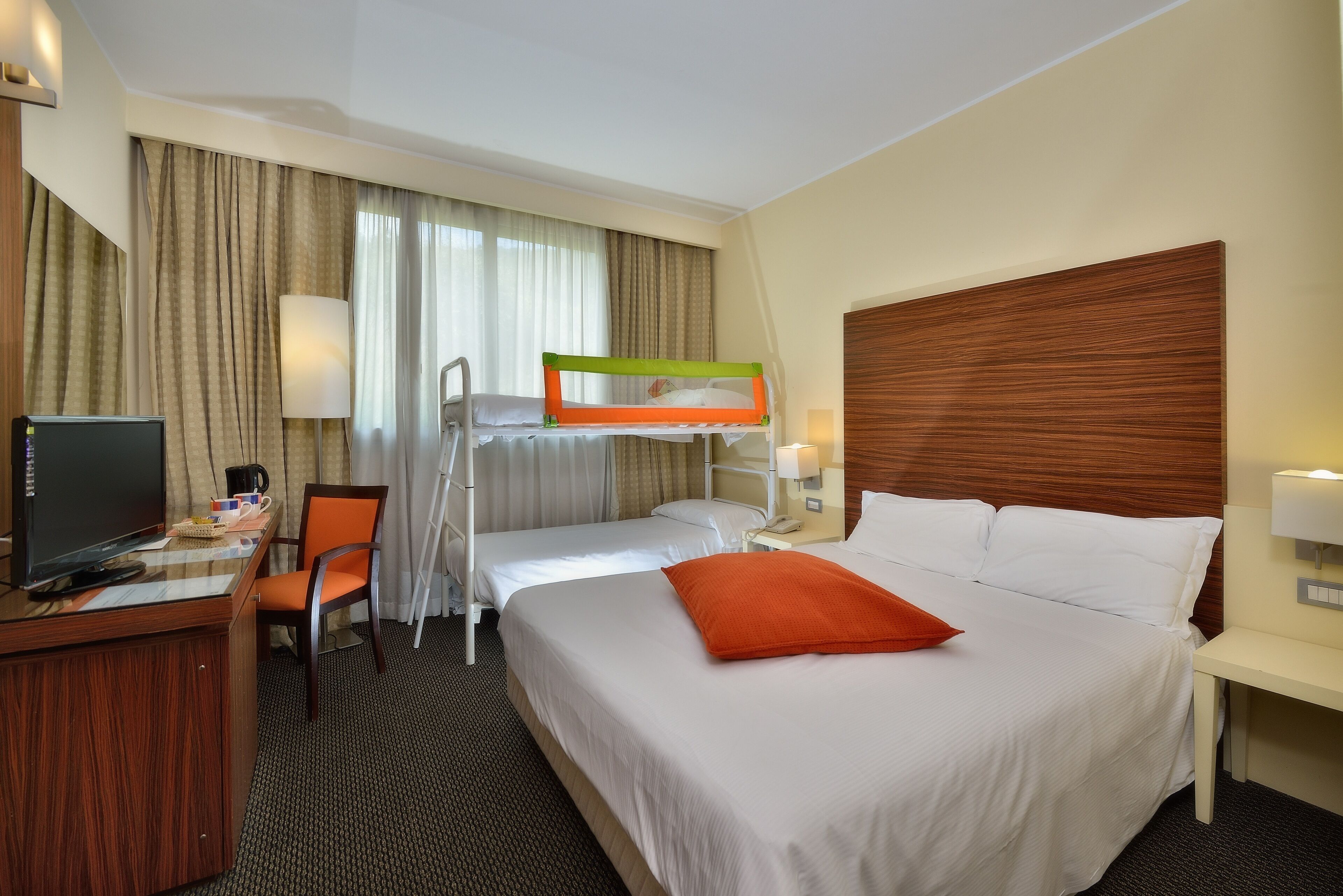 A hotel room with a bunk bed, a desk with a computer, a chair, and a TV.