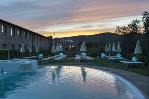 A pool area with lounge chairs and umbrellas, surrounded by a building and hills in the background. - La Meridiana Bleisure Hotel (Perugia)