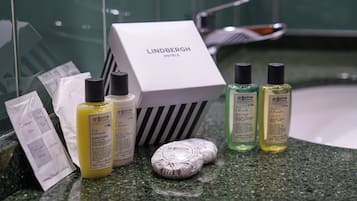 A bathroom counter with toiletries including a Lindbergh Hotels box, bottles of Bigelow conditioner, and toiletries.