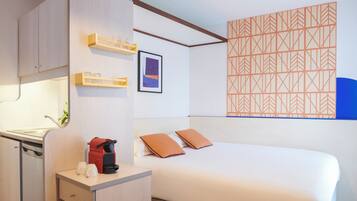 A hotel room with a bed, a desk with a coffee maker, a small cabinet, and a wall with a geometric pattern.