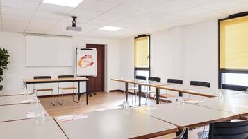 Una sala de conferències amb taules, cadires, un projecte, una pissarra i una planta.