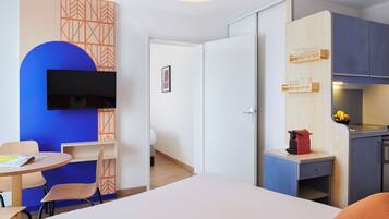 Une chambre comprenant un lit, un bureau, une chaise, une télévision et un coin cuisine.