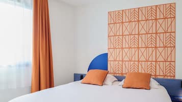 Ett hotellrum med en säng, gardiner, en vägg med mönster och en taklampa.