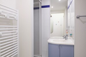 A bathroom with a white sink, blue cabinets, a glass shower enclosure, and a towel rack. - Aparthotel Adagio Access Rennes Centre (Rennes)