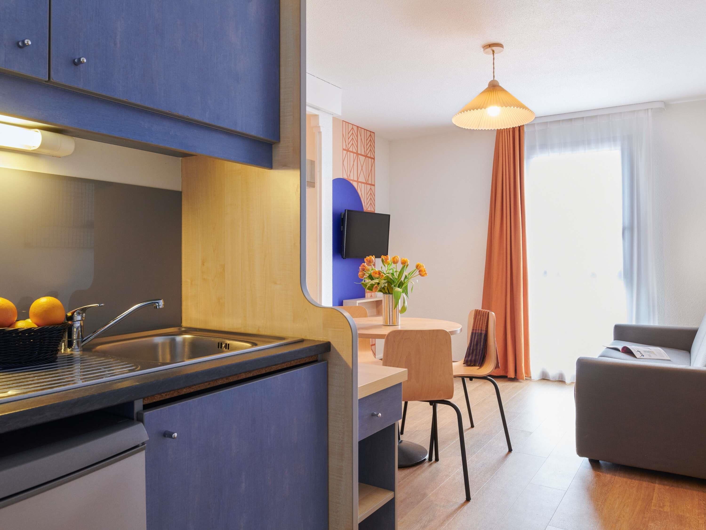 Una cocina moderna con un lavamanos, un comedor con mesa y sillas, y una sala de estar con sofá.