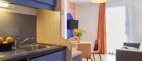A modern kitchen with a sink, a dining area with a table and chairs, and a living area with a sofa.