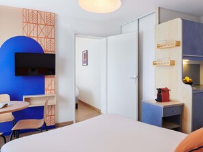 A hotel room with a bed, a desk with a computer, a TV mounted on the wall, and a kitchenette area. - Aparthotel Adagio Access Rennes Centre (Rennes)