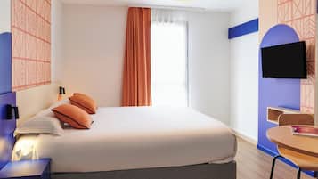 A hotel room with a bed, a desk, a chair, a TV, and a window with curtains.