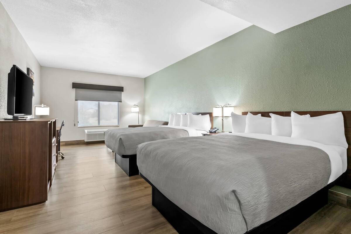 A hotel room with two beds, a TV, a desk, and a window.