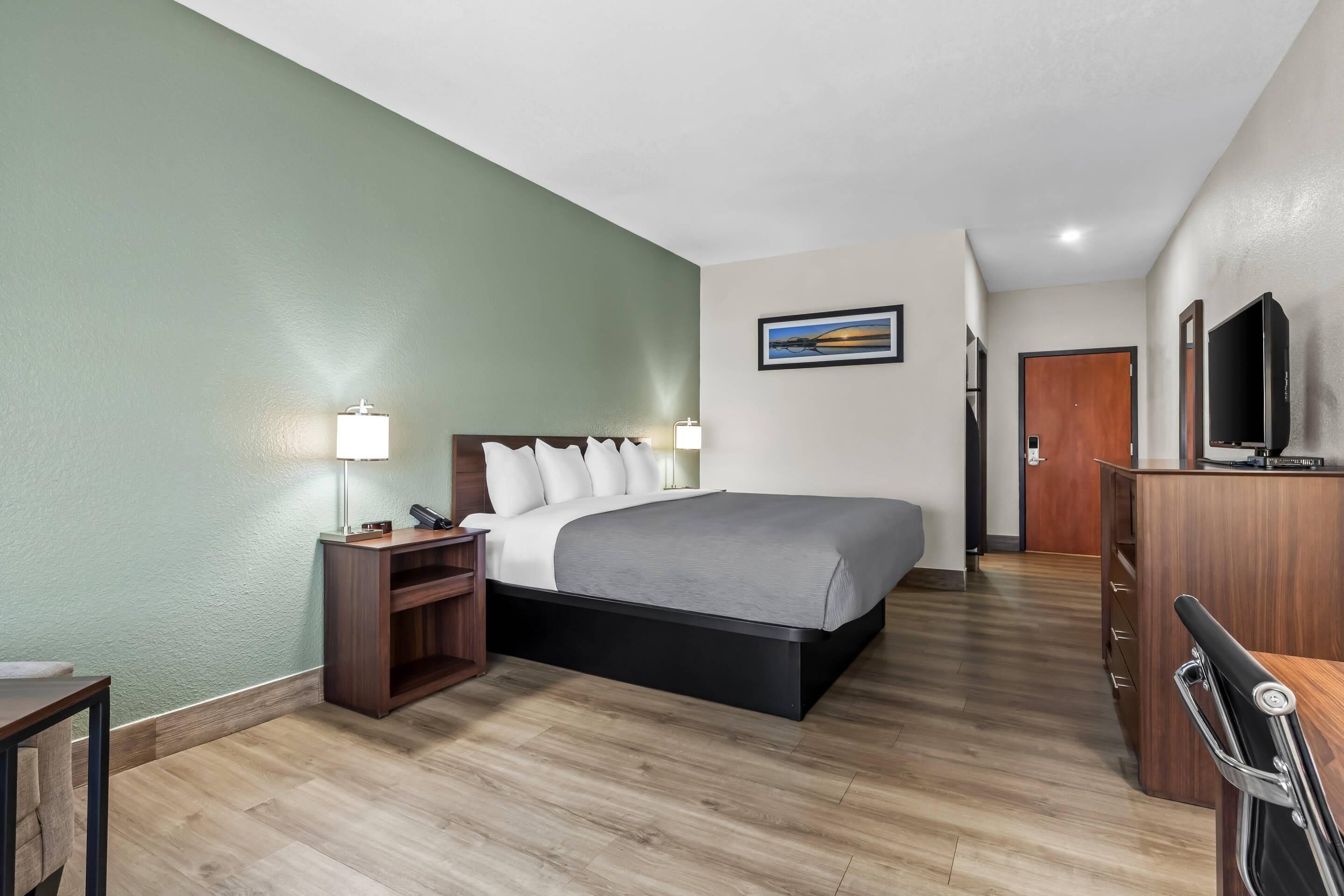 Una habitación de hotel con cama, mesita de noche, lámpara, televisor y cómoda de madera.