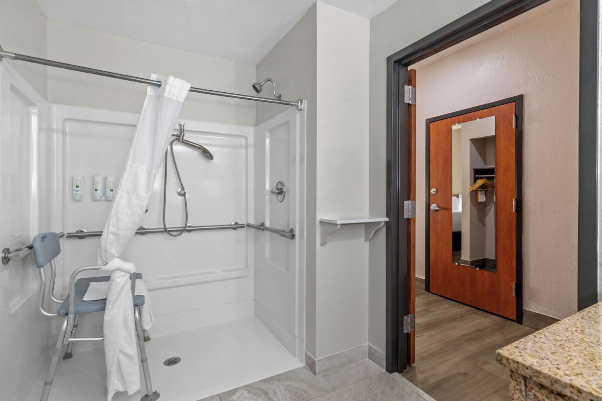 A wheelchair-accessible shower with a glass door, a handrail, and a showerhead.