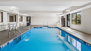 Une piscine intérieure avec des parois en verre transparent, une terrasse carrelée et une vue sur les arbres à travers de grandes fenêtres.