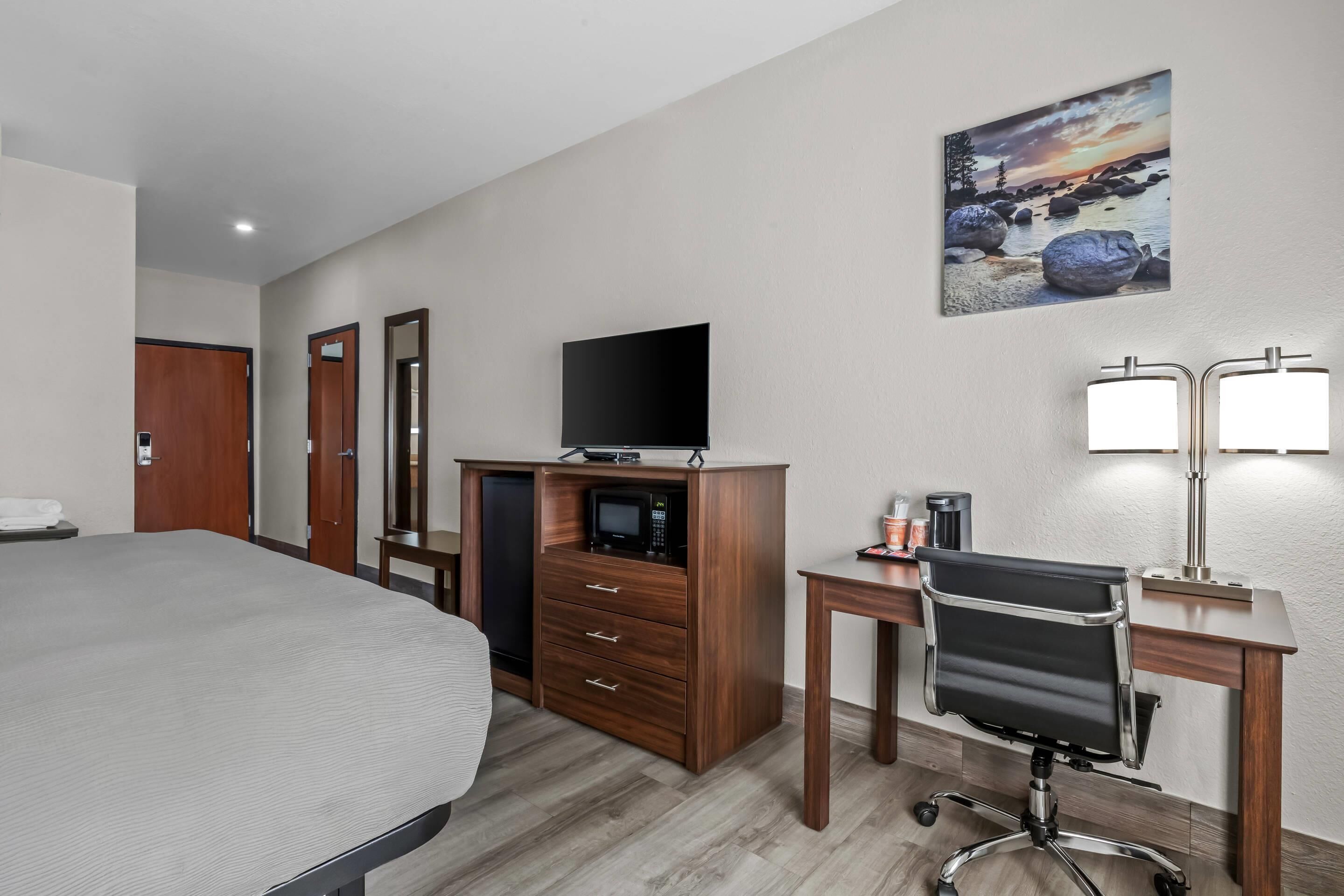 Habitación de hotel con cama, escritorio con silla, televisión, cómoda y un cuadro en la pared.