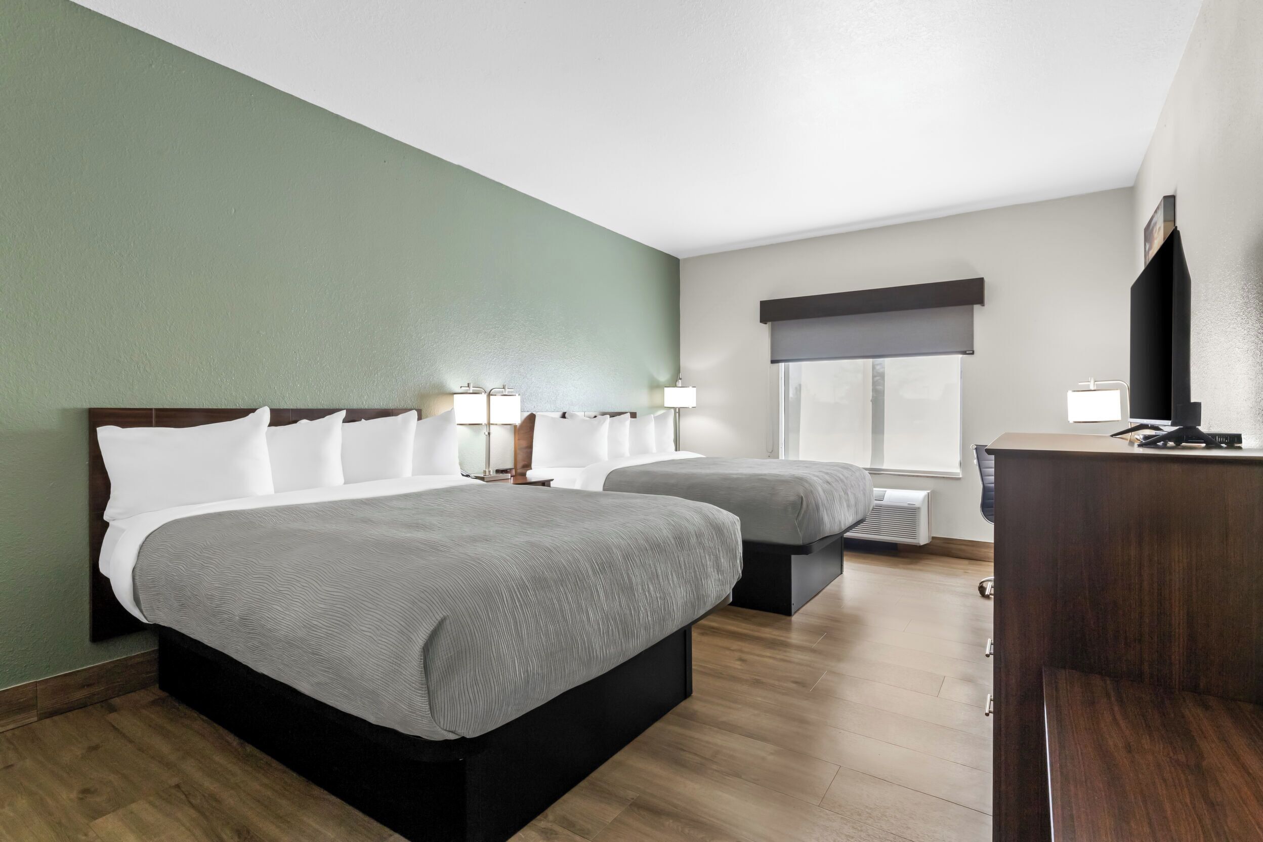 A hotel room with two beds, a desk, a TV, and a window with a view.