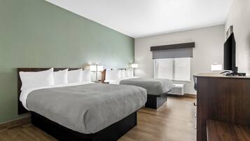 A hotel room with two beds, a desk, a TV, and a window with a view.