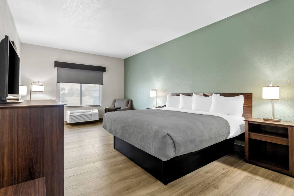 A modern hotel room with a large bed, bedside lamps, a desk, and a chair.