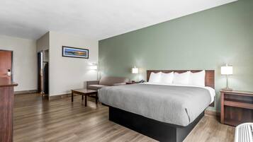 Quarto de hotel com cama, cadeira, escrivaninha, abajur e quadro na parede.