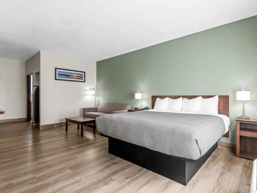 Quarto de hotel com cama, cadeira, escrivaninha, abajur e quadro na parede.
