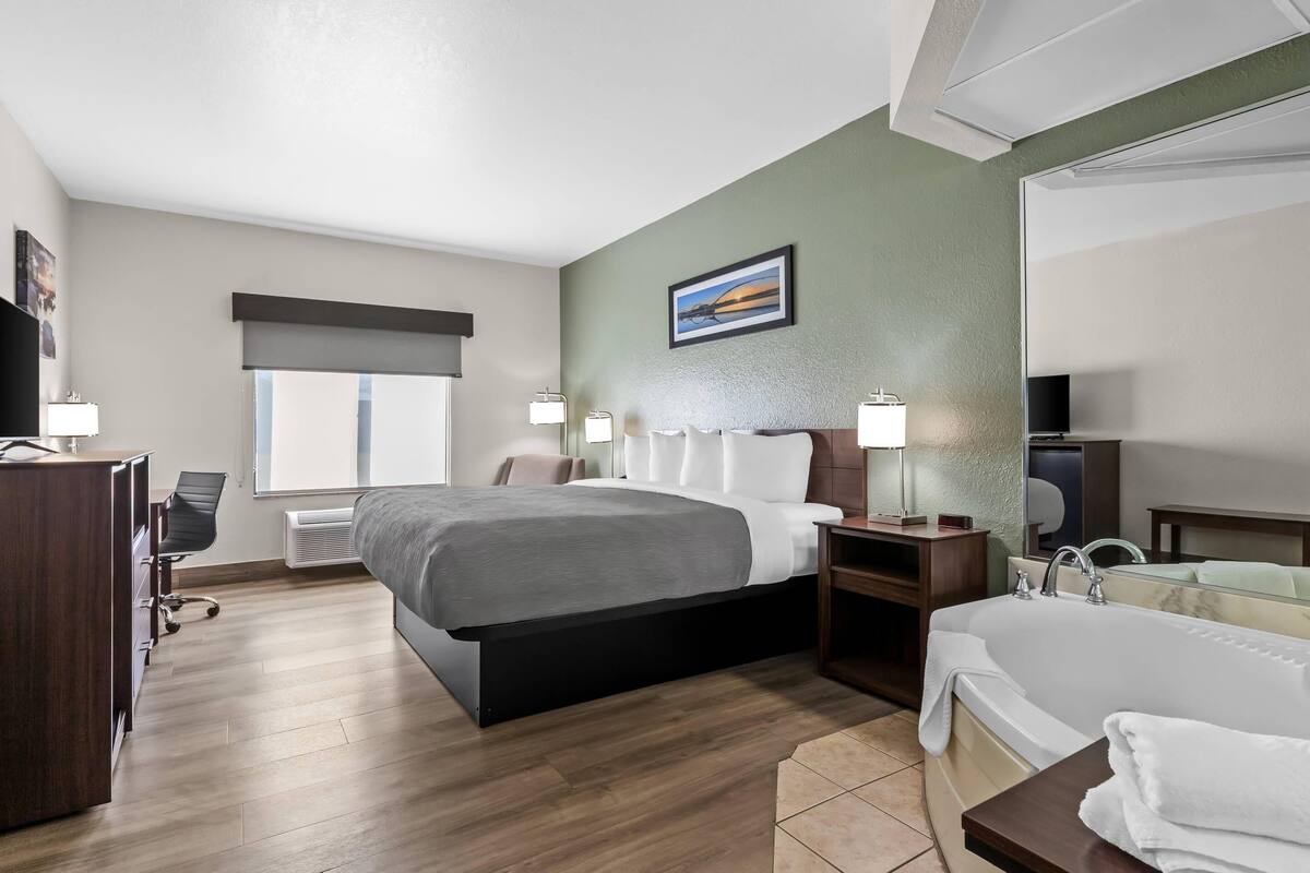 A hotel room with a bed, bedside table, lamp, TV, and a bathroom with a bathtub.