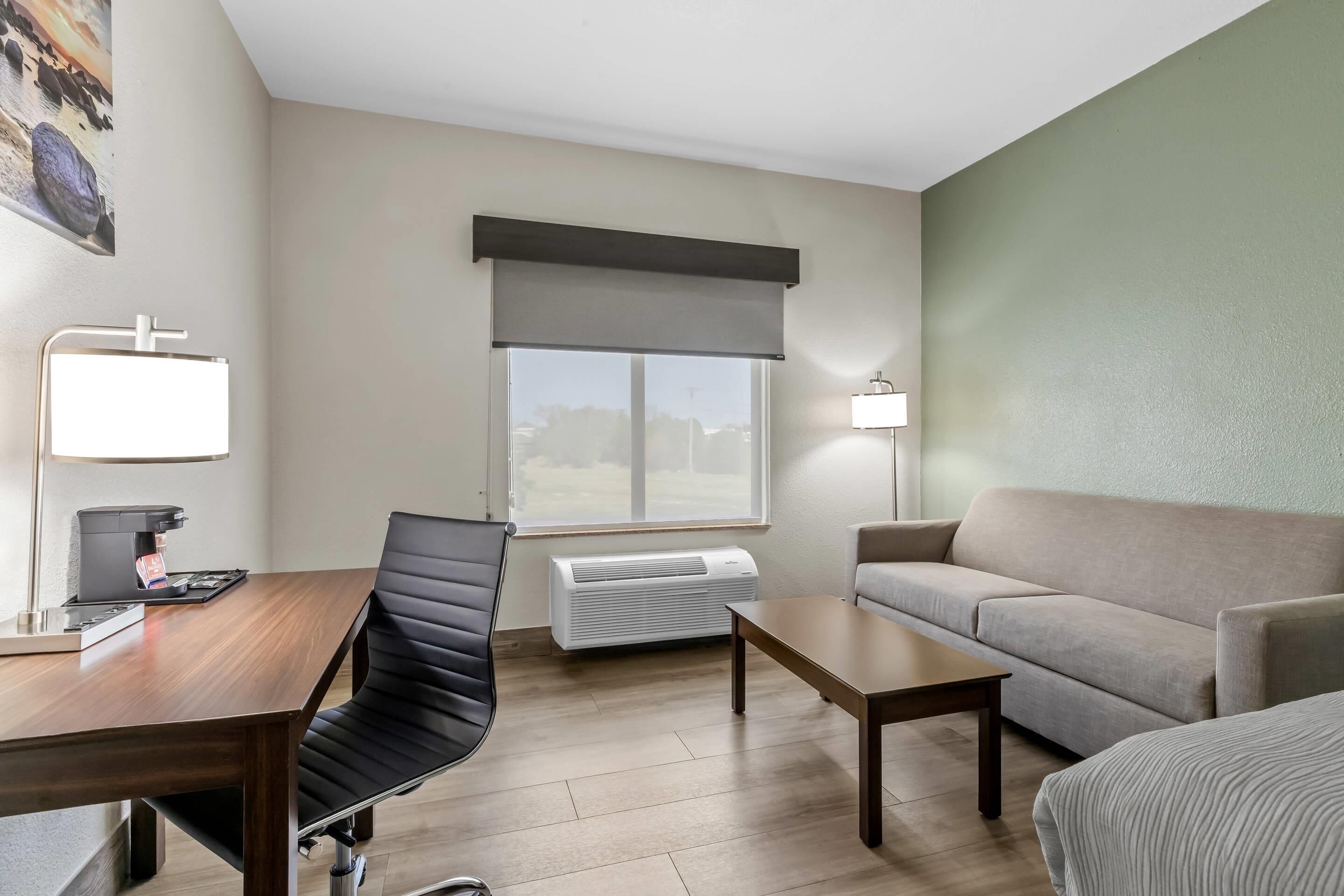 Una habitación de hotel con escritorio, silla, sofá y ventana con vistas.