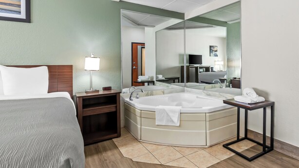 Une chambre d’hôtel avec un lit, un grand miroir, une baignoire, une petite table et une table de chevet.