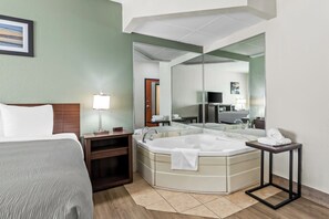 A hotel room with a bed, a large mirror, a bathtub, a small table, and a nightstand. - Quality Inn Tahlequa South (Tahlequah)