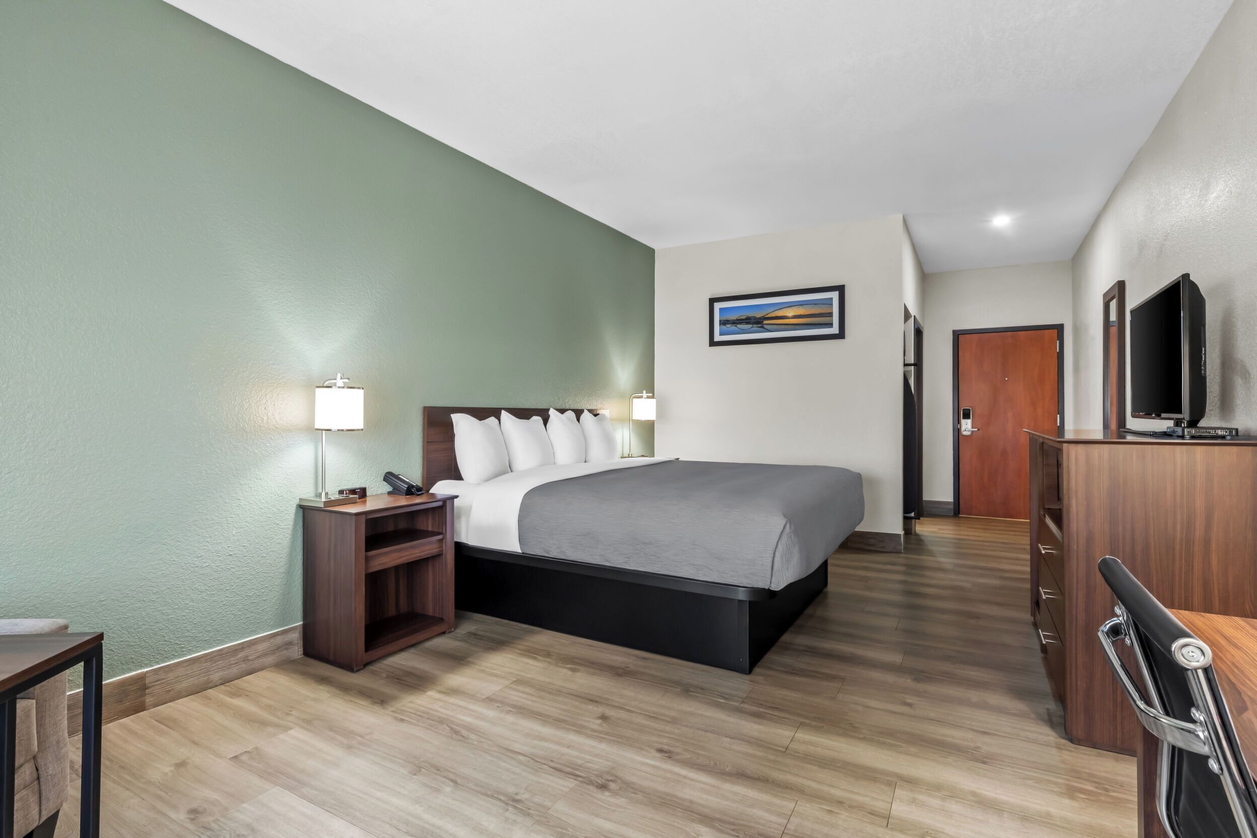 A hotel room with a bed, bedside tables, a desk, a television, and a door.