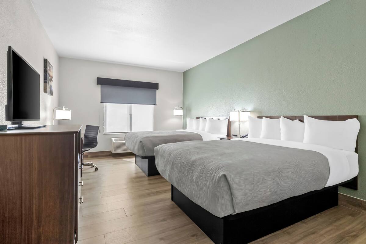 A hotel room with two beds, a desk, a TV, and a window with a view.