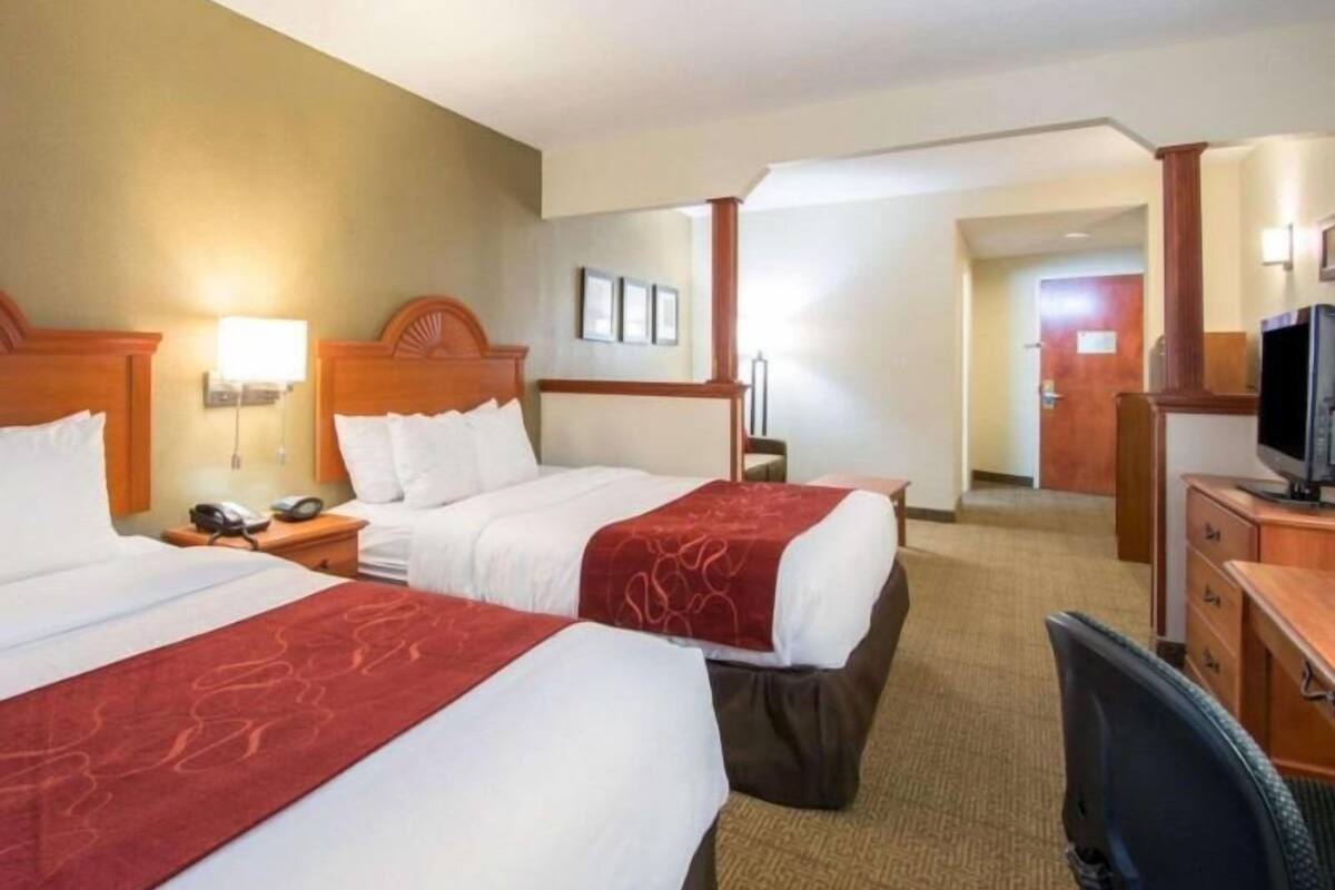 A hotel room with two beds, a desk, a chair, a television, and a door leading to another room.