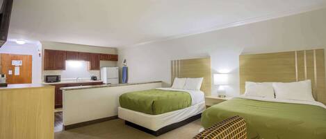 A hotel room with two beds, a kitchenette, a TV, and a small seating area.