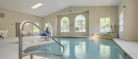 An indoor swimming pool with clear water, a metal ladder, and a bench.