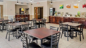 A dining area with multiple tables and chairs, a kitchen area with a refrigerator, and a wall with food-related pictures.