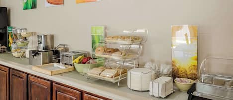 Un bufé de desayuno con diversas opciones de comida, una máquina de café y un bol de fruta.