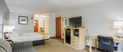 Habitación de hotel con cama, escritorio con computadora, televisor, sofá y una pequeña kitchenette.
