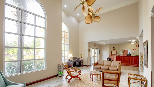A spacious lobby with a large arched window, a reception desk, a seating area with a sofa and chairs, and a kitchen area in the background.