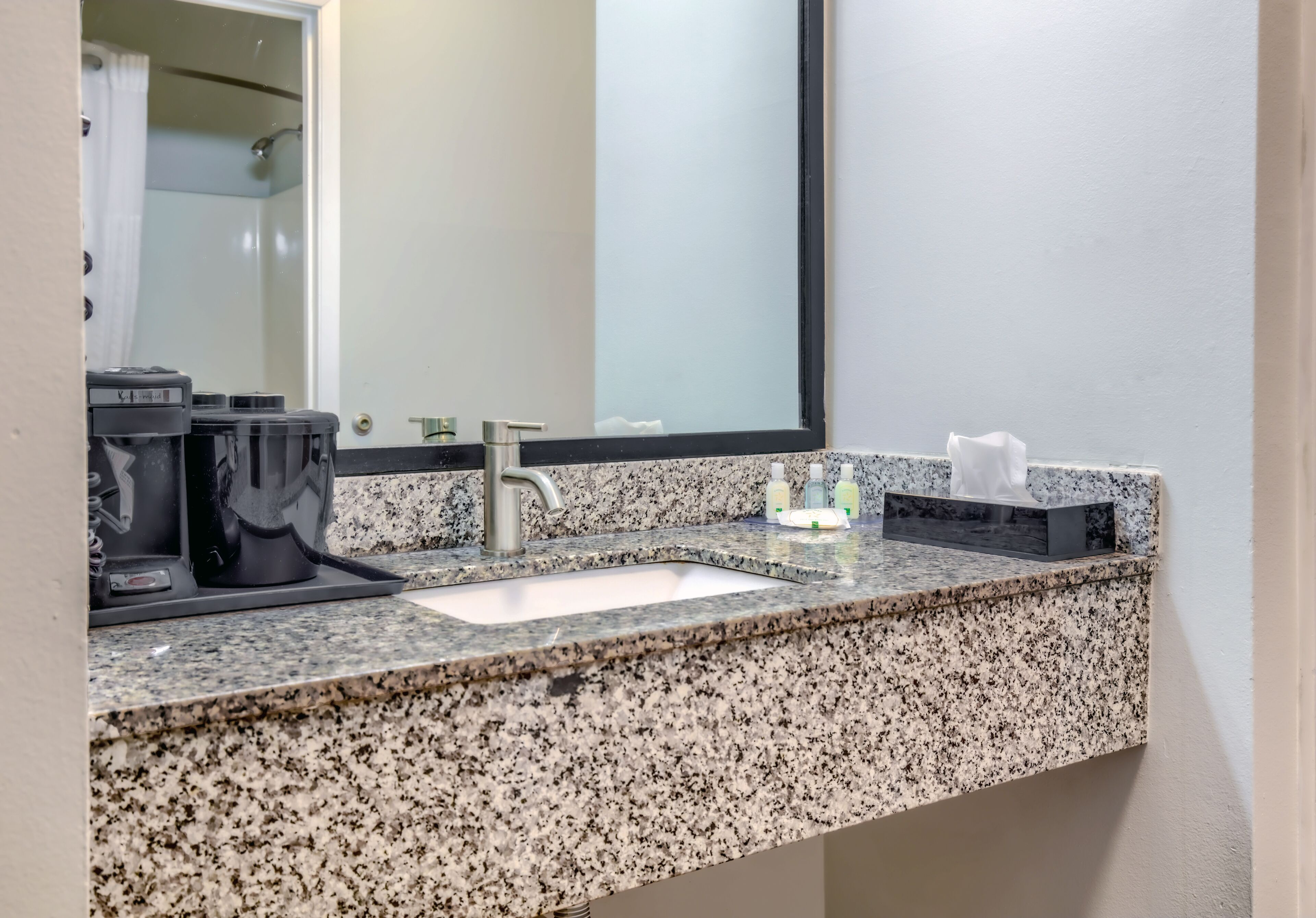 Une salle de bain avec un comptoir en granit, un lavabo, un miroir et des articles de toilette.