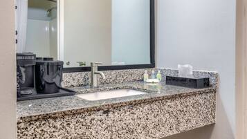 Une salle de bain avec un comptoir en granit, un lavabo, un miroir et des articles de toilette.