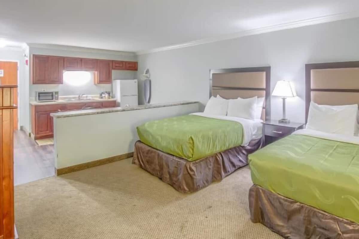 A hotel room with two beds, a kitchenette, and a bathroom.