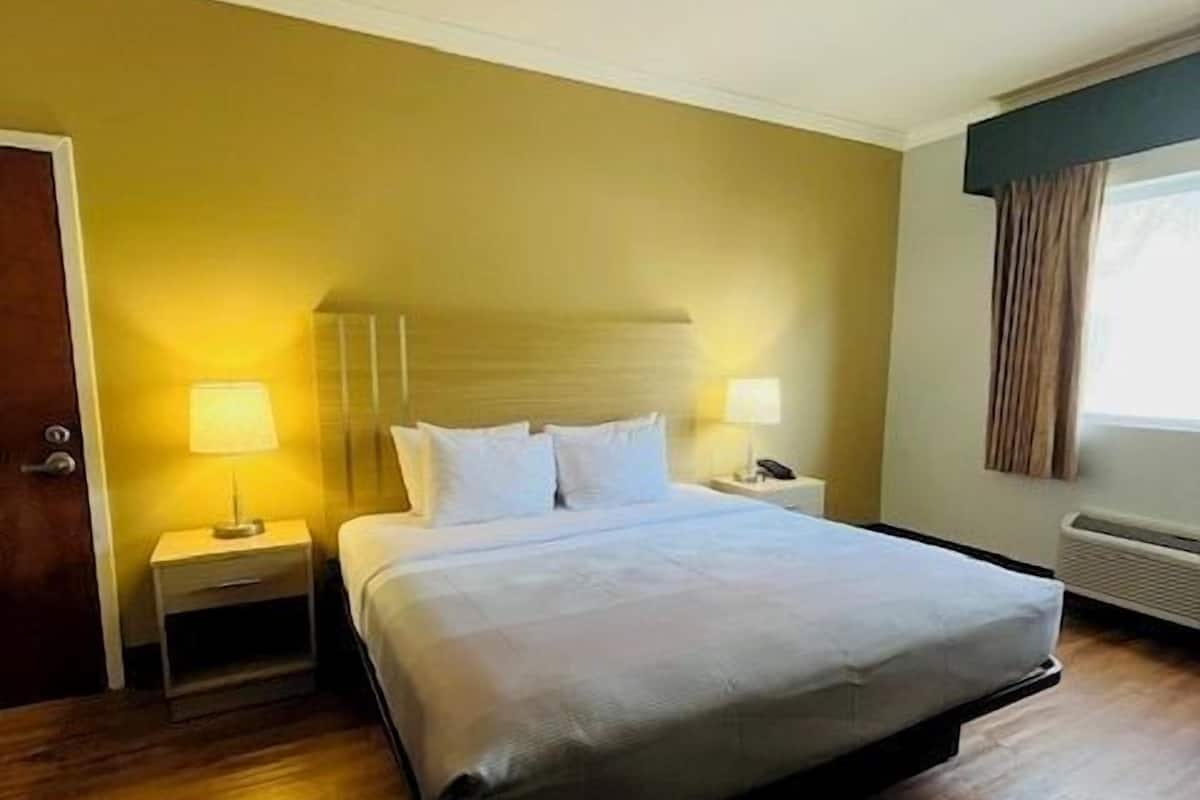 A hotel room with a bed, two bedside tables, a nightstand, a door, and a window with curtains.