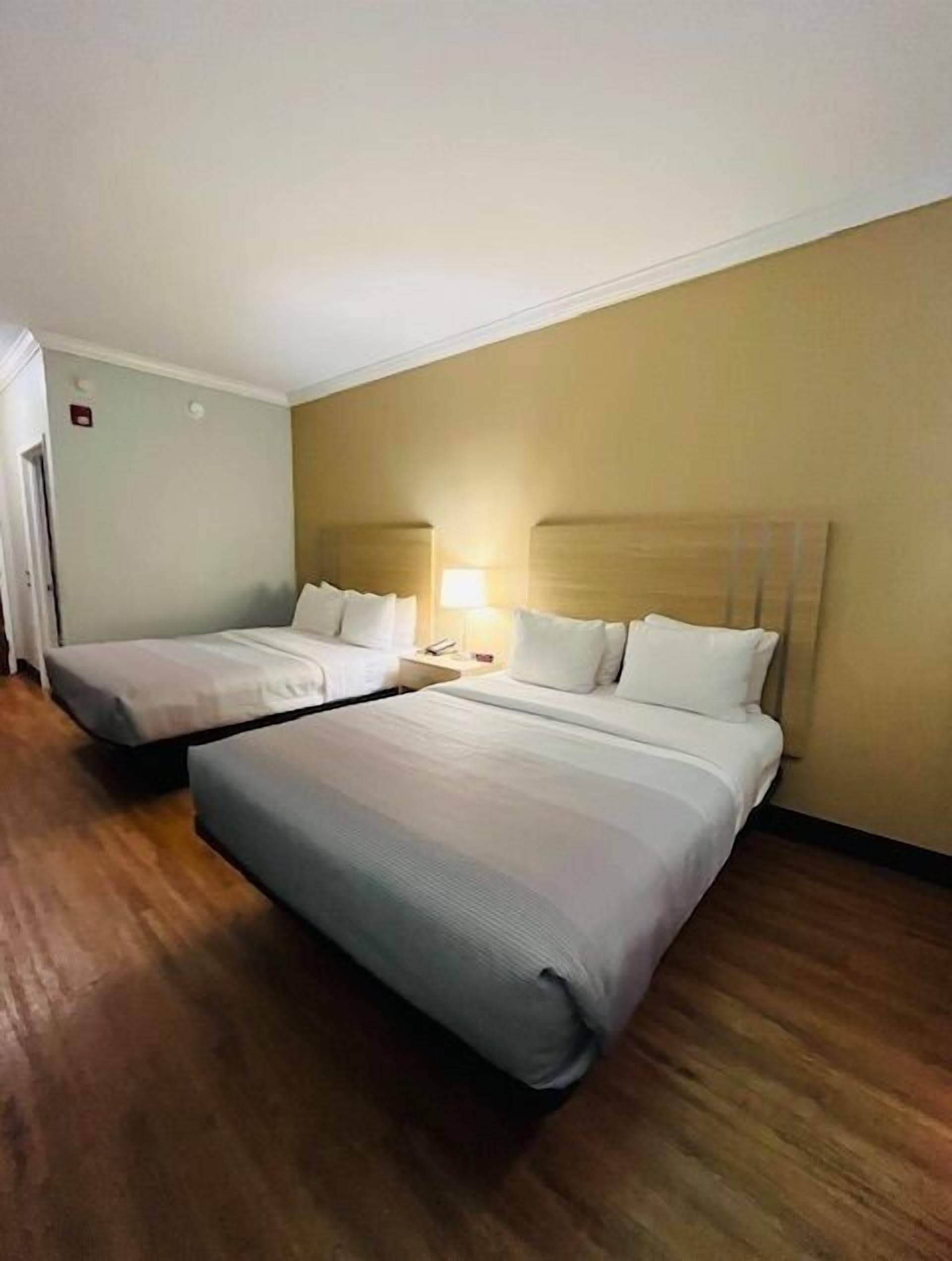 A hotel room with two single beds, wooden flooring, and a beige wall.