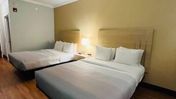 A hotel room with two single beds, wooden flooring, and a beige wall.
