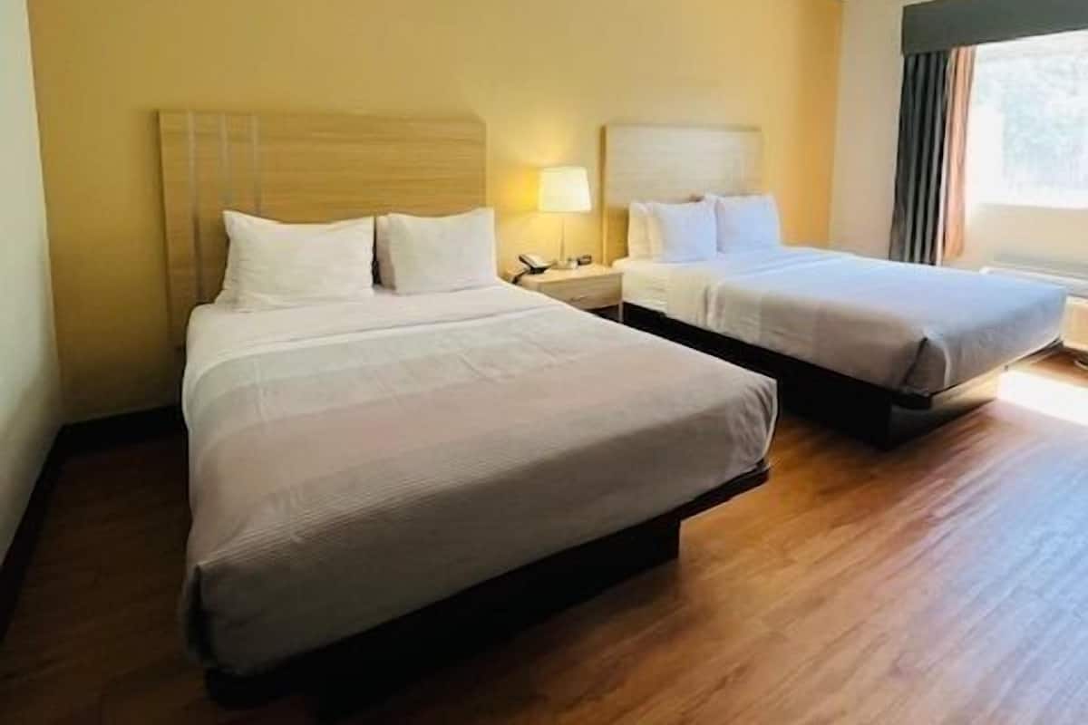 A hotel room with two beds, wooden flooring, and a window with curtains.
