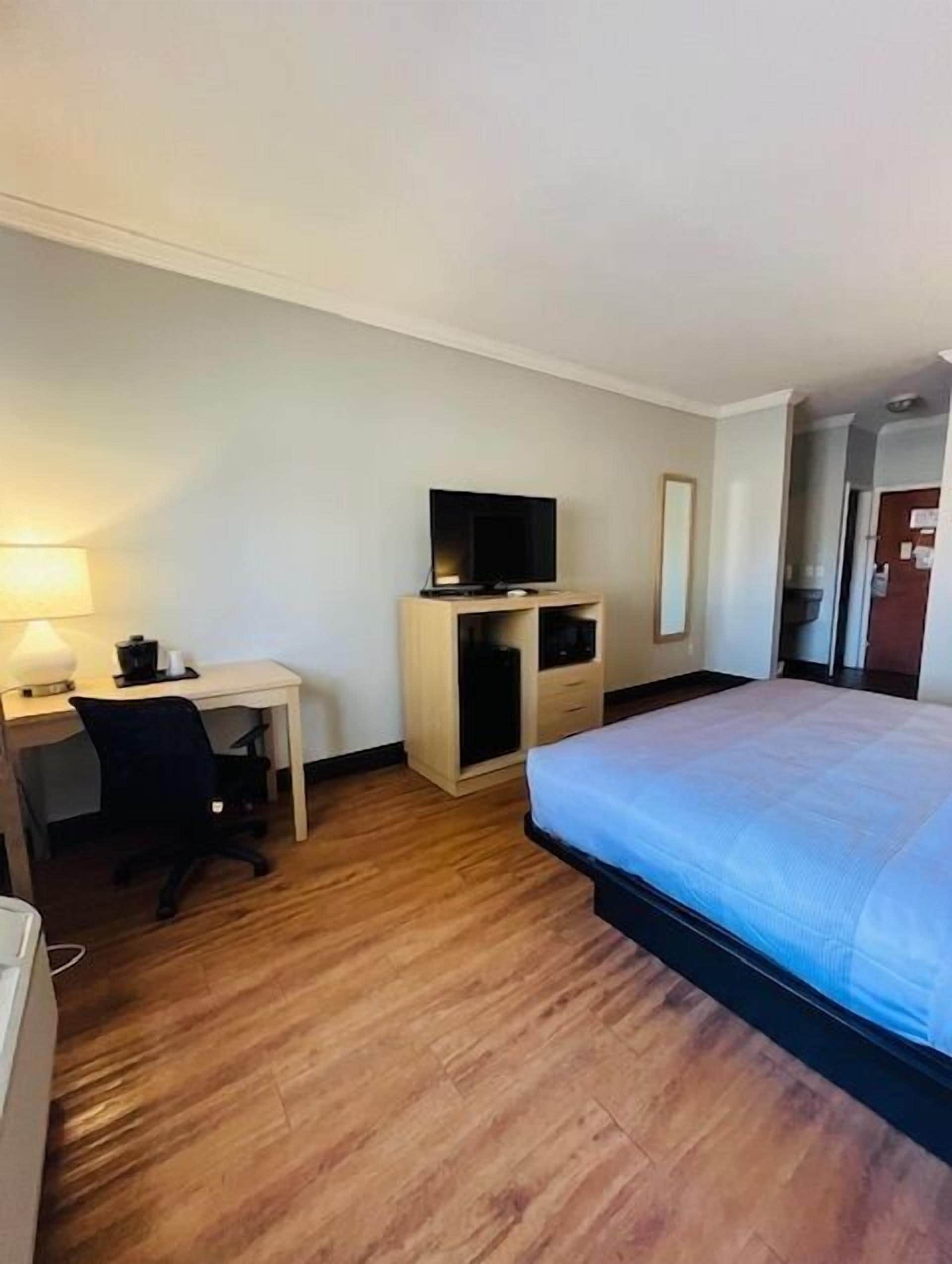 Habitación de hotel con cama, escritorio y silla, televisor, armario y lámpara.