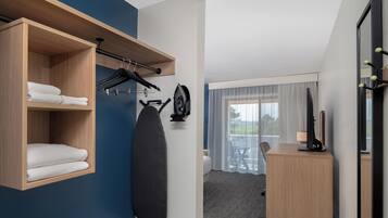 Habitación de hotel con repisa de madera con toallas, tabla de planchar negra y escritorio con lámpara.