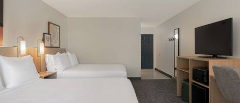 A hotel room with two beds, a desk with a computer, a TV, and a microwave.
