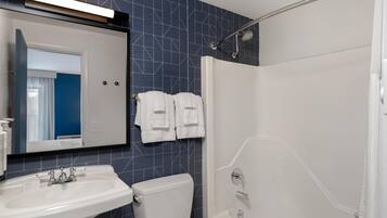 Une salle de bain avec un lavabo blanc, des toilettes, une douche avec une porte en verre et un miroir au-dessus du lavabo.