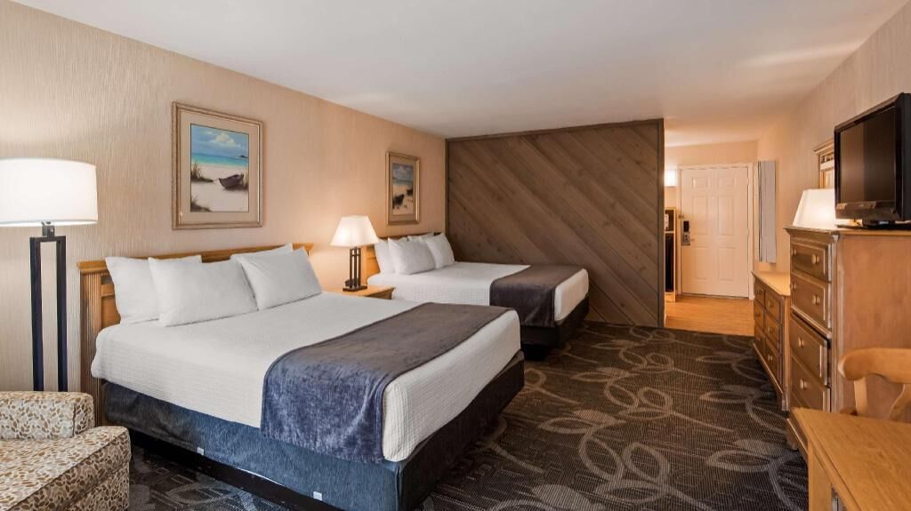 A hotel room with two beds, a desk, a television, and a patterned carpet.