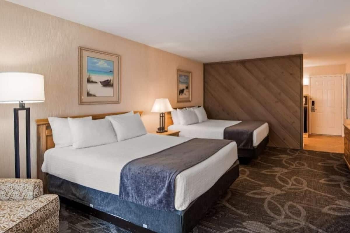 A hotel room with two beds, a desk, a television, and a patterned carpet.